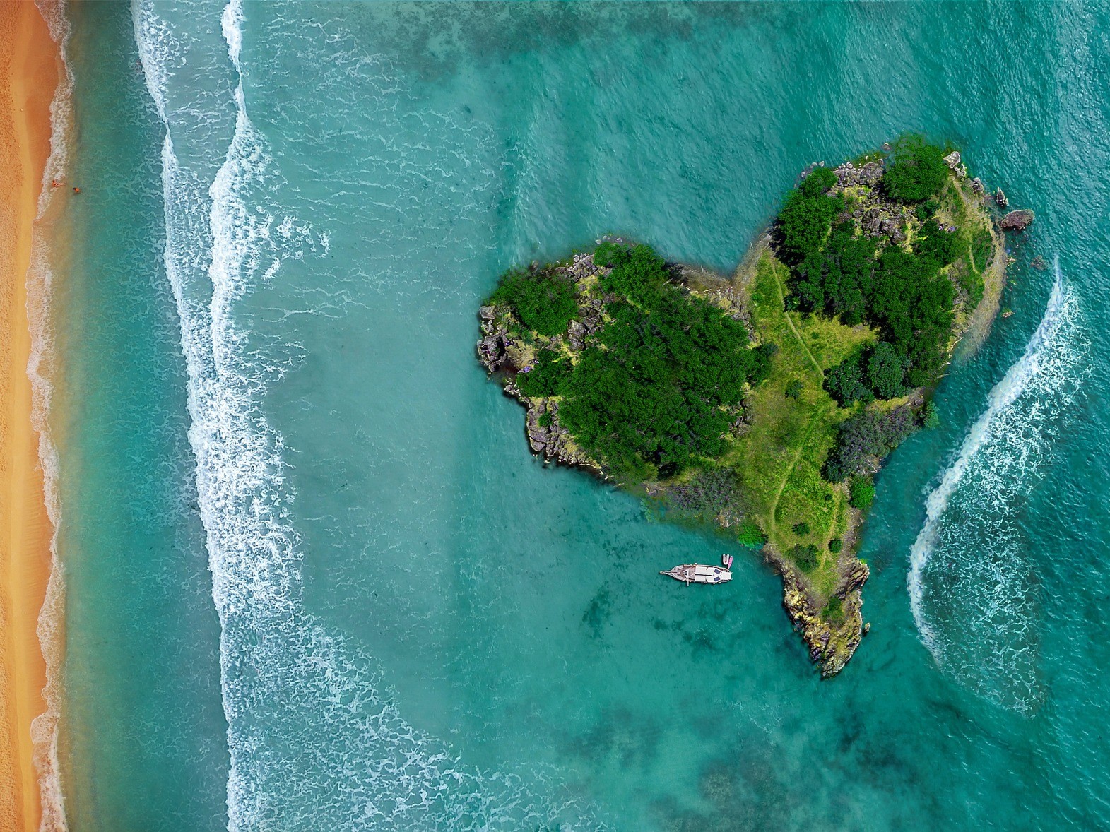 Luftaufnahme einer herzförmigen, bewaldeten Insel im türkisblauen Wasser neben einem Sandstrand, mit einem kleinen Boot das an der Küste ankert
