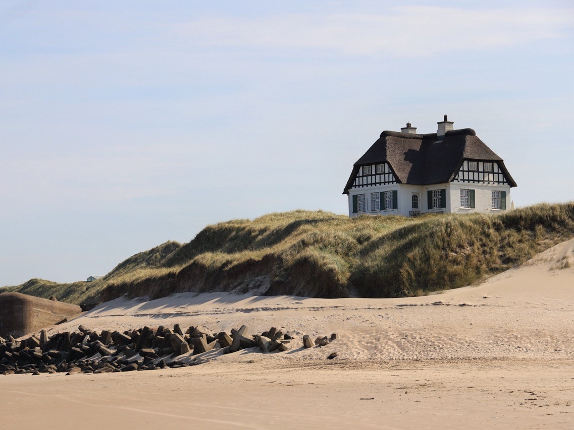 Historisches Reetdachhaus mit Fachwerk auf einer Düne an der dänischen Nordseeküste, umgeben von Stranddünen mit Dünengras und Wellenbrechern am Sandstrand – Küstengrundstück Aurea Dune, 2 Hektar, zum Verkauf über ISLA AURUM