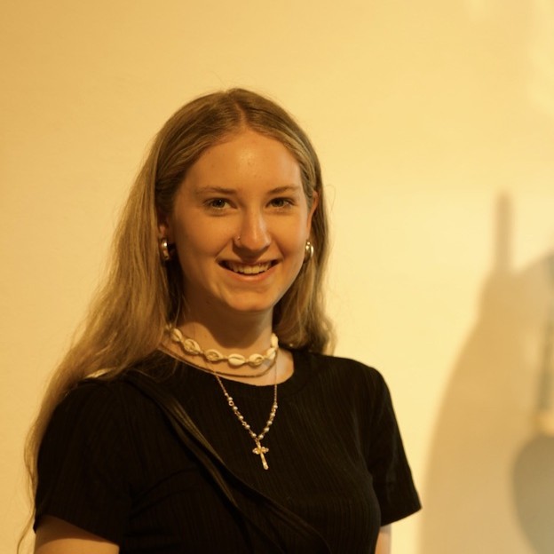 Porträtfoto einer lächelnden jungen Frau mit langen blonden Haaren und einer Kette vor hellem Hintergrund